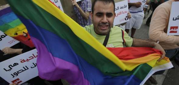 A protestor waves the gay pride flag as others hold banners during an anti-homophobia rally in Beirut on April 30, 2013. Lebanese homosexuals, human rights activists and members from the NGO Helem (the Arabic acronym of "Lebanese Protection for Lesbians, Gays, Bisexuals and Transgenders") rallied to condemn the arrest on the weekend of three gay men and one transgender civilian in the town of Dekwaneh east of Beirut at a nightclub who were allegedly verbally and sexually harassed at the municipality headquarters. AFP PHOTO/JOSEPH EID (Photo credit should read JOSEPH EID/AFP/Getty Images)