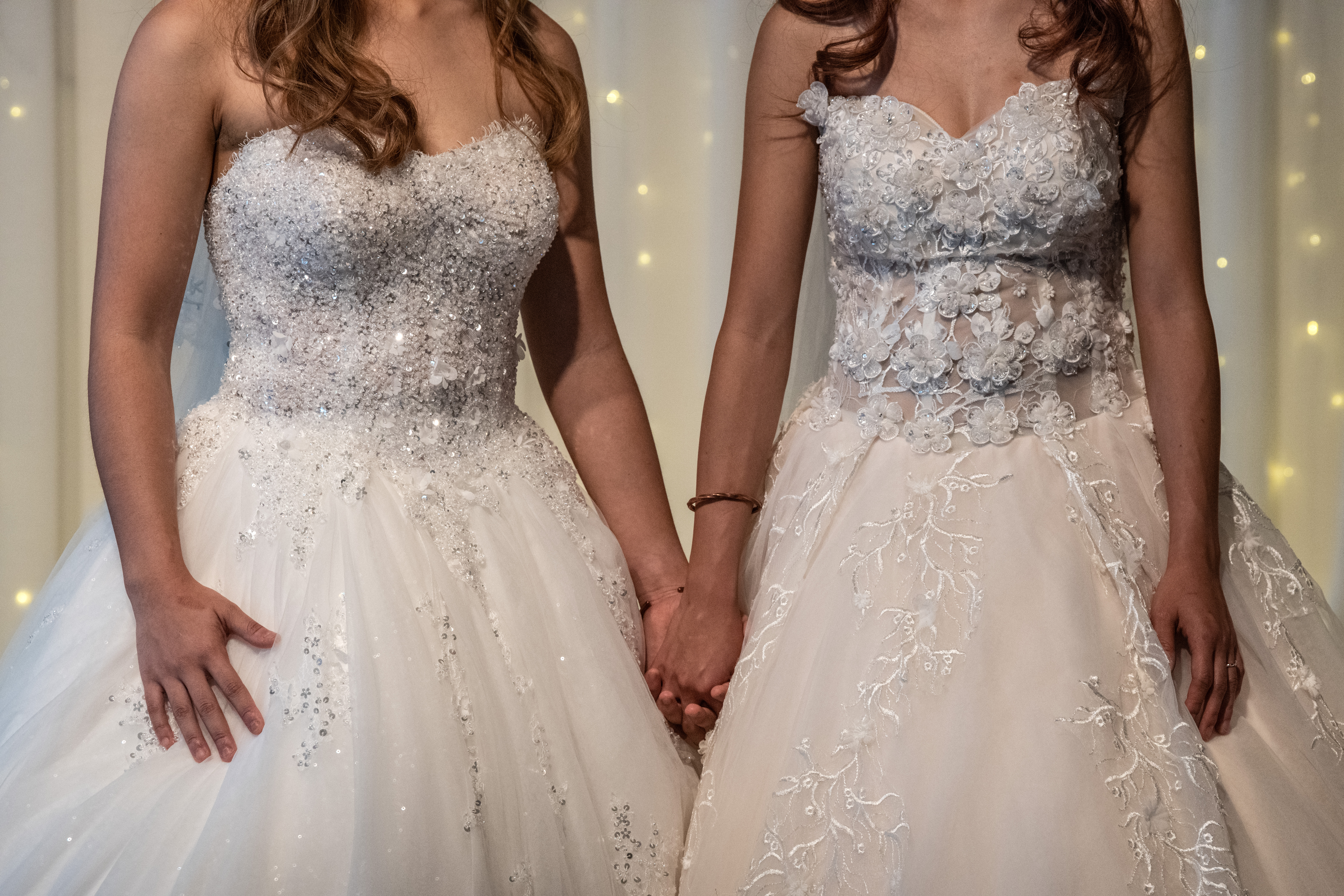 Lesbian couple hold hands wearing wedding dresses.