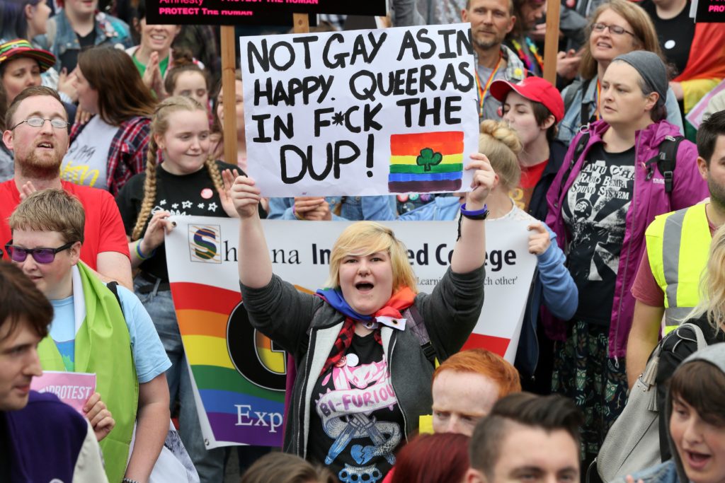 A protestor holding a sign that says: "Not gay as in happy. Queer as in f*ck the DUP"