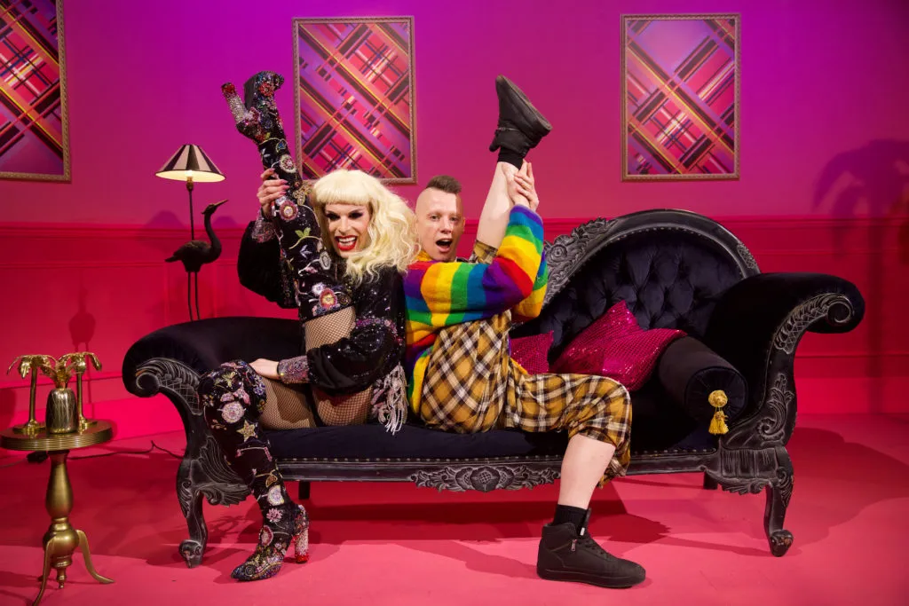 Drag Race queens Katya and Divina holding their legs in the air.