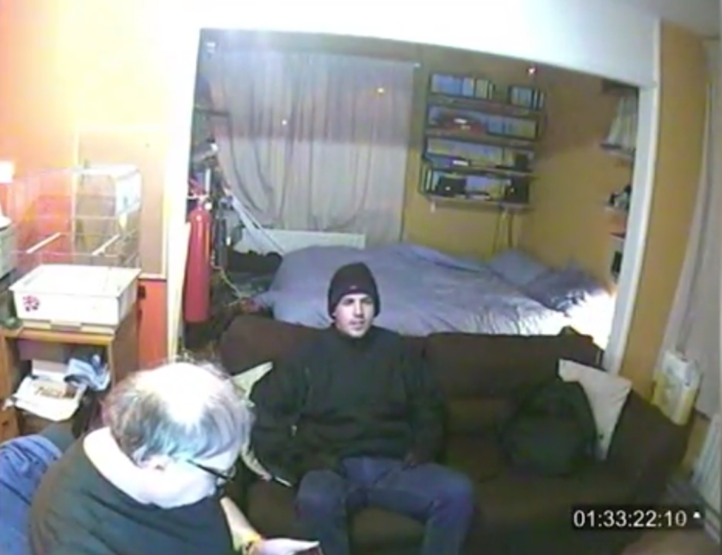 Jason Marshall, dressed as an MI5 agent, chats to Peter Fasoli in his West London apartment. (Screen capture via Metropolitan Police) 