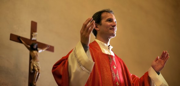 Catholic priest on altar praying with open arms during mass service in church. (Stock photo via Elements Envato)