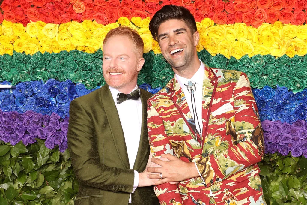 Jesse Tyler Ferguson and his husband Justin Mikita in front of a rainbow flower wall