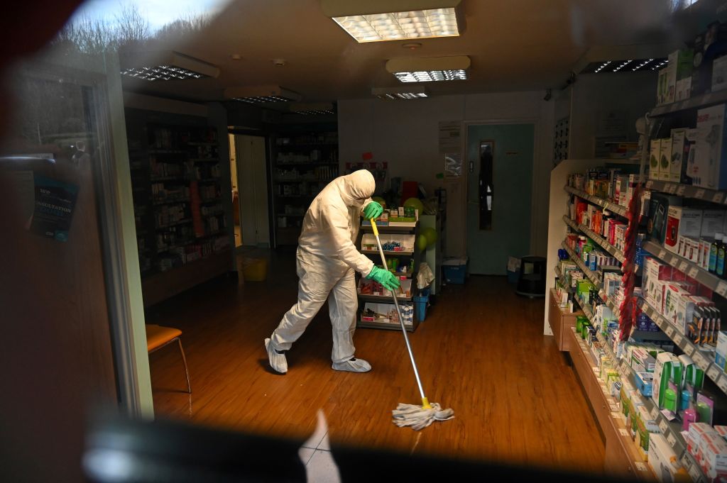 A worker in protective clothing, including face mask and gloves, is pictured cleaning the floor of a pharmacy