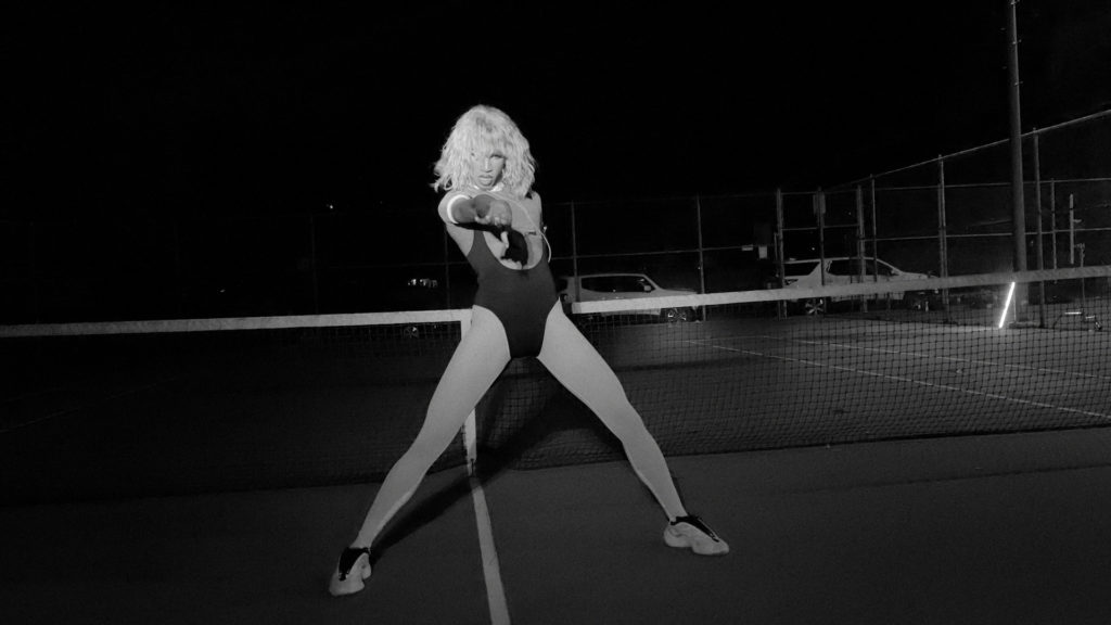 Black and white image of Naomi Smalls on a tennis court, in a leotard and white tights