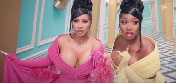 Cardi B and Megan Thee Stallion walking down a twist Alice in Wonderland-style corridor in gowns in the WAP video