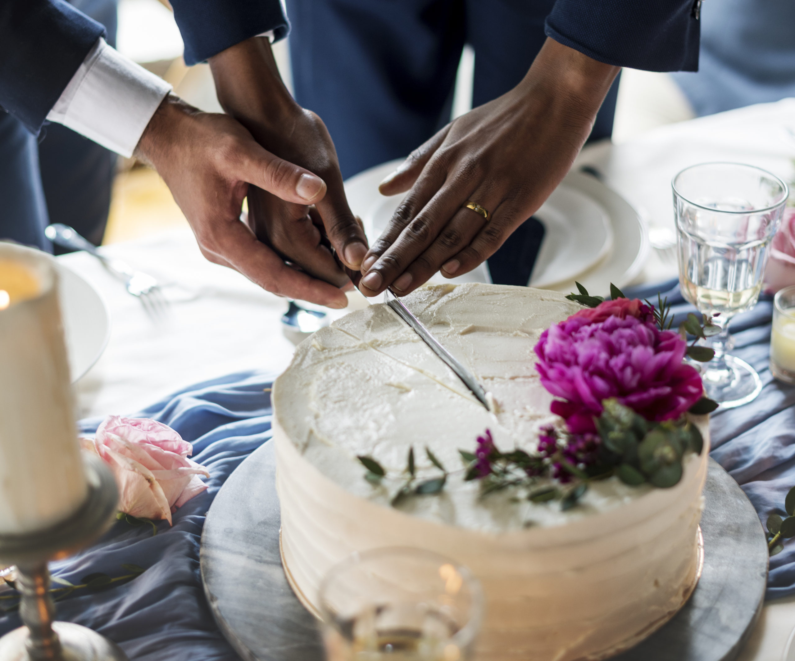 Close-up of two male hands cutting a wedding cake