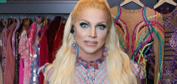 Courtney Act in a drag closet with a rail of glittering dresses behind her