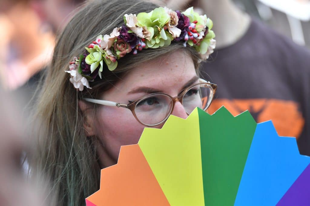 A woman with a flower crown peeps over a rainbow-coloured fan