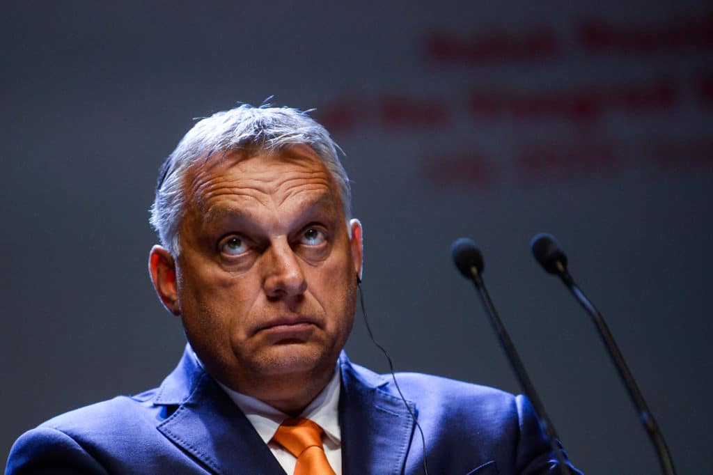 Viktor Orbán in a navy suit and orange tie looks up while at a press conference