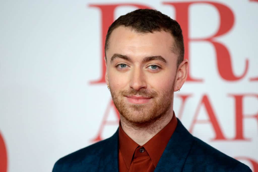 Sam Smith smiles in a buttoned-up burgundy shirt and black blazer