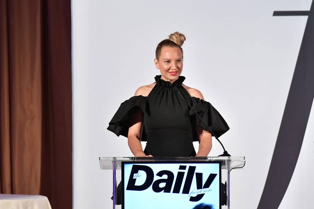 Sia with her hair in a top knot, speaking at a podium 