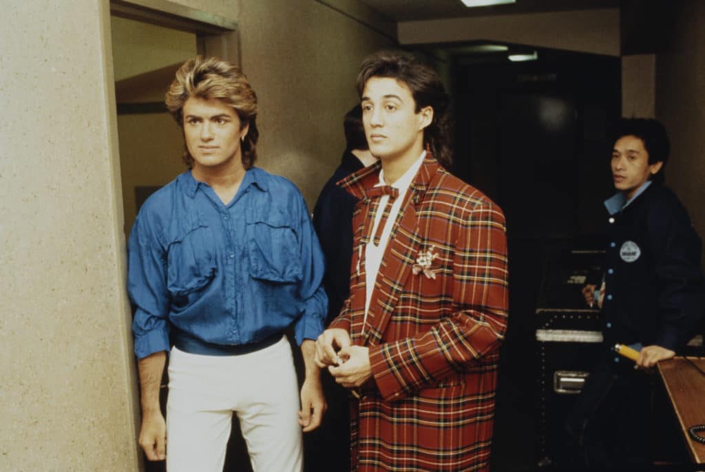 George Michael in a denim shirt and white jeans and Andrew Ridgeley in a tartan suit