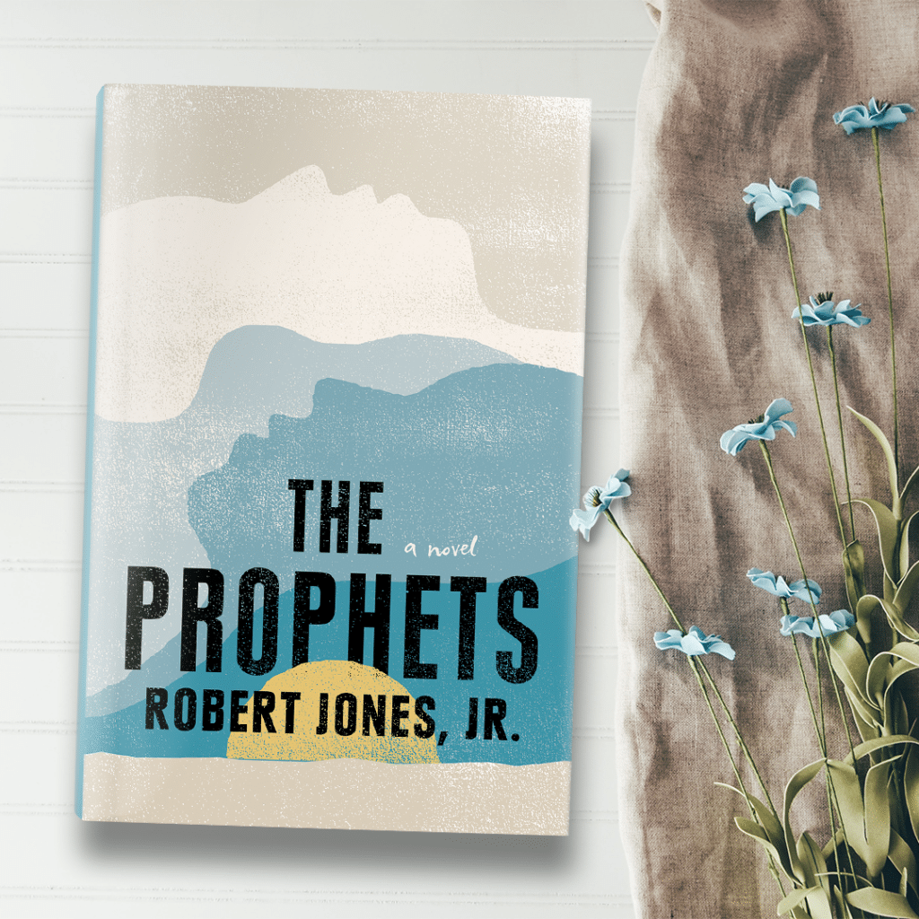 A hardback copy of The Prophets. Its cover is a simple illustration of a sunset. Next to the book are blue flowers.