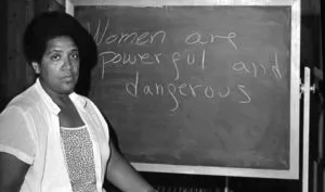 Audrey Lorde standing in front of a chalkboard with the message 'women are powerful and dangerous'