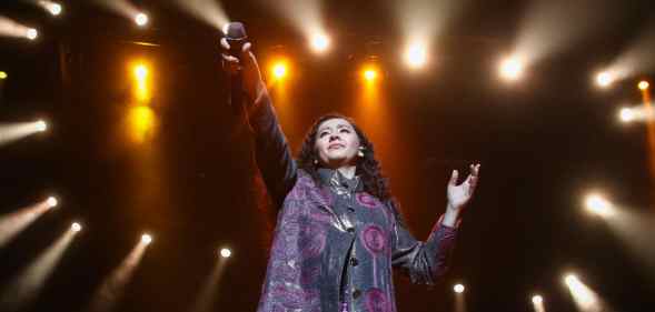 Manizha Sangin holds her microphone in the air against a constellation of spotlights