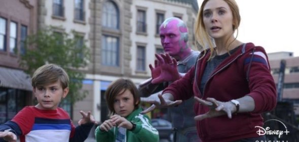 Superheros Wanda and Vision with their two young children, Billy and Tommy, all standing in a street with their hands raised, ready to attack