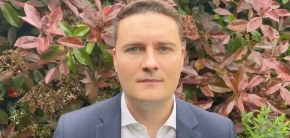 Wes Streeting wearing a shirt and blazer in front of a bush