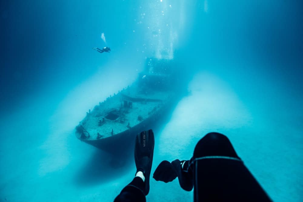 Picture of a person's feet underwater with shipwreck visible