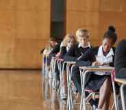 Teenage Students In Uniform Sitting Examination In School Hall