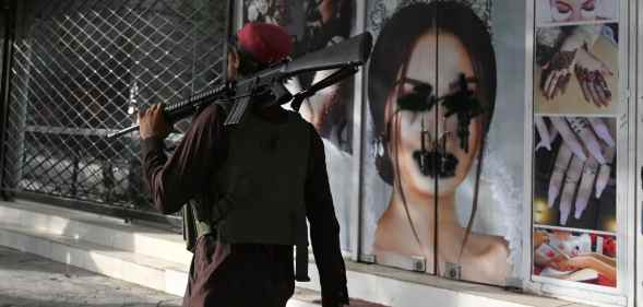 A Taliban fighter walks past a beauty salon with images of women defaced.