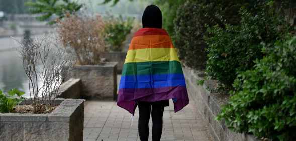 Student with LGBT+ flag draped over their shoulders, photographer from behind, in Beijing, China