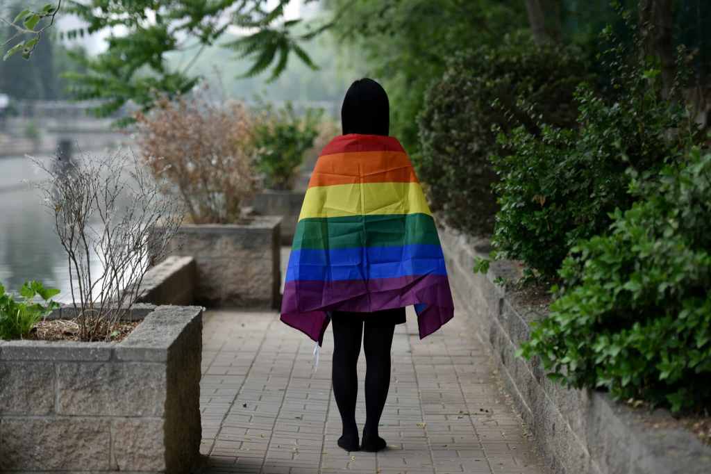 Student with LGBT+ flag draped over their shoulders, photographer from behind, in Beijing, China