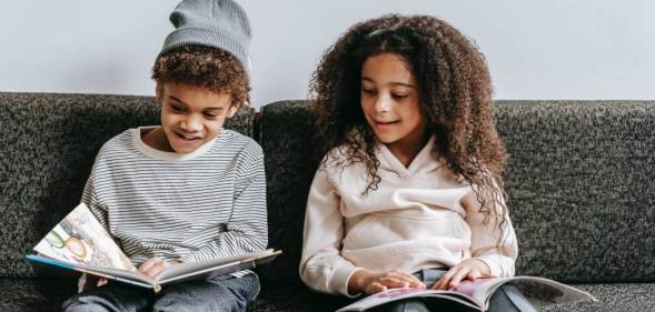 Two children are sitting on a couch and reading books