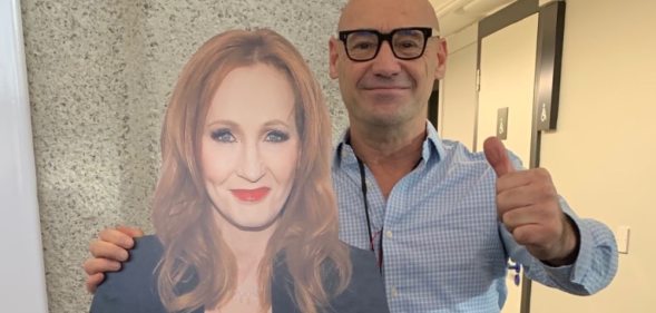 A bald man stands next to a cardboard cutout of JK Rowling