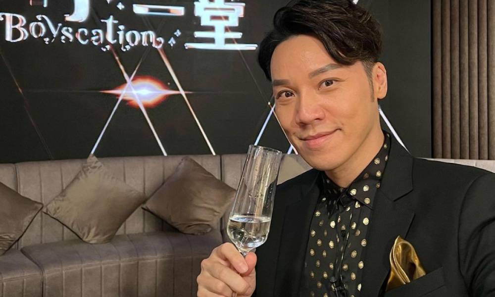 Vinci Wong sits with a glass of some kind of celebratory drink in front of black background with the word Boyscation on it