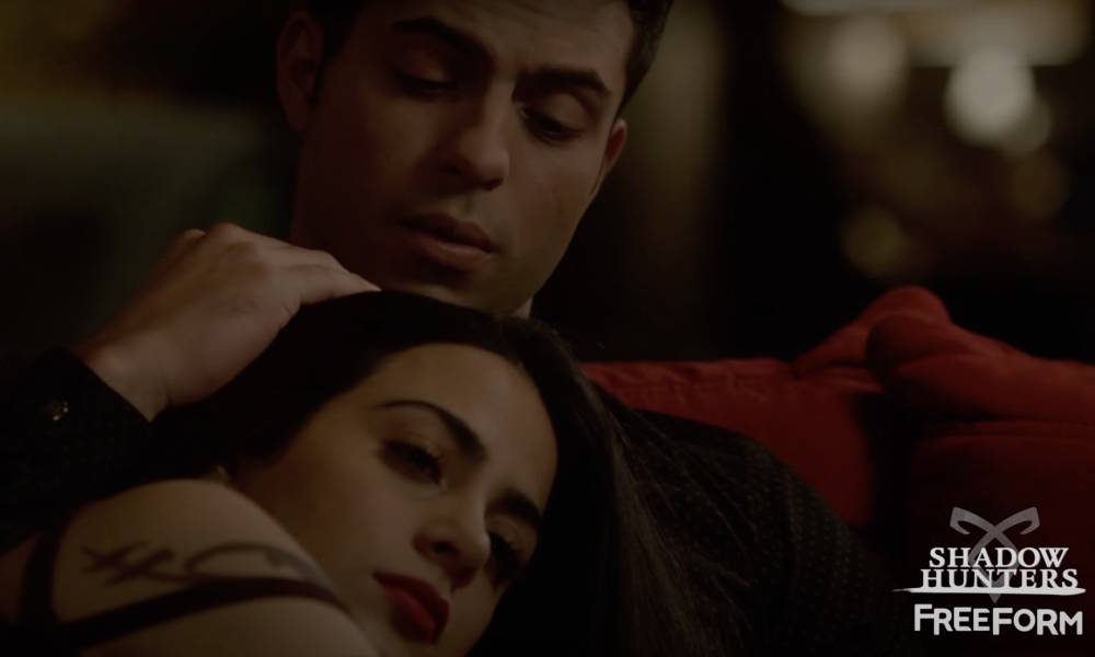Shadowhunters characters Raphael Santiago and Isabelle Lightwood are cuddled on a coach in an episode from the second season of the show