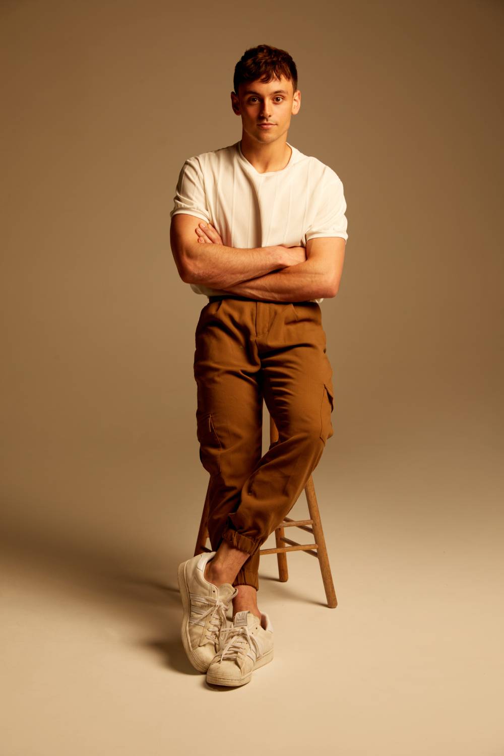 Tom Daley sits on a stool in front of a neutral background