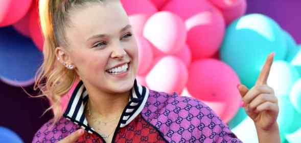 JoJo Siwa stands in front of colourful balloons while wearing red and purple jacket