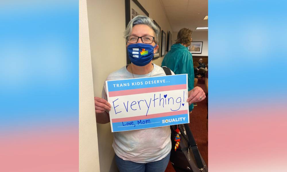 Hillary Moore-Embry holds up a sign that reads "Trans kids deserve everything love mom"