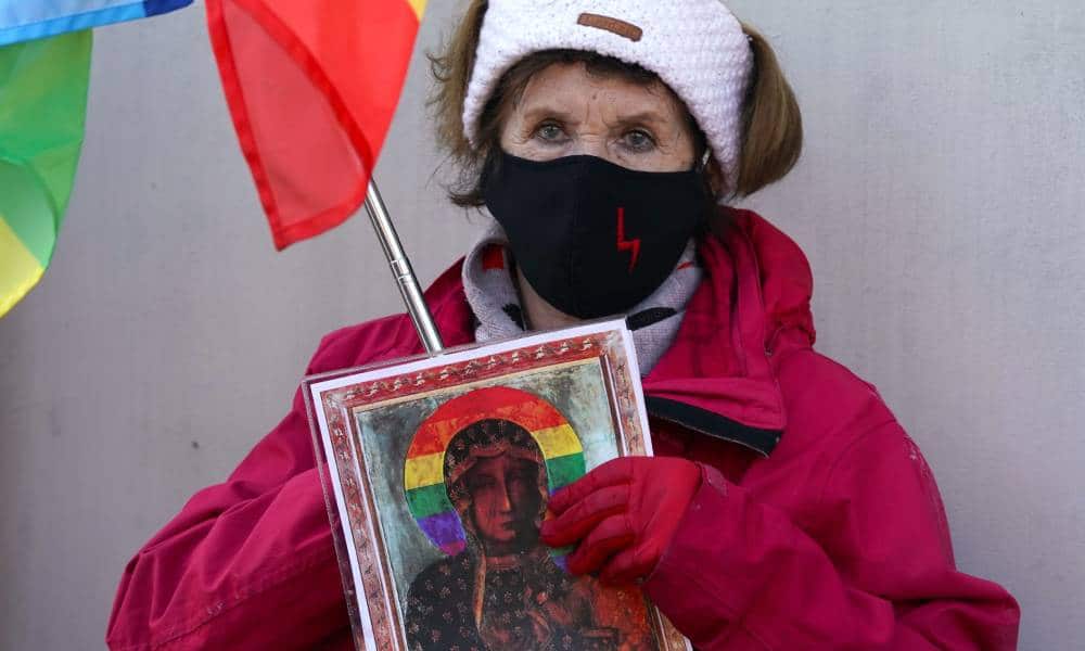 A supporter dressed in red coat and a black face mask holds up a photo of the Virgin Mary with a rainbow halo