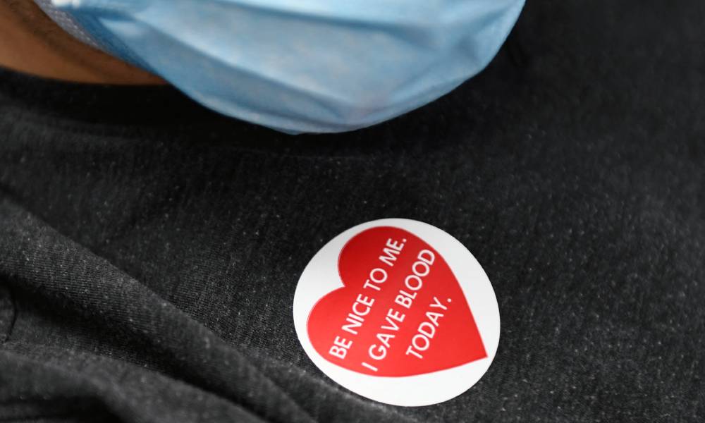 A person wearing a face mask and a sticker on their t-shirt donates blood