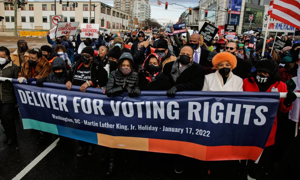 Member of Martin Luther King Jr's family and civil rights advocates march with a banner that reads "deliver for voting rights"