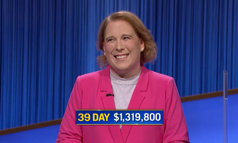 Jeopardy! champion Amy Schneider wears a pink top and darker pink jacket as she smiles after she wins her 39th consecutive game