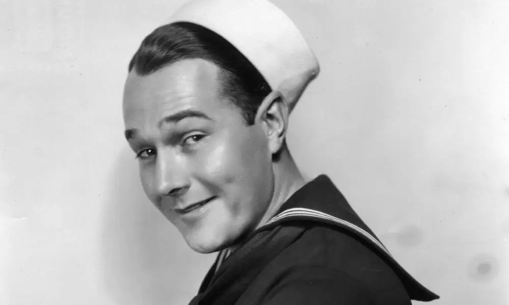 William Haines, a silent film star, wears a sailor costume in a black and white photo