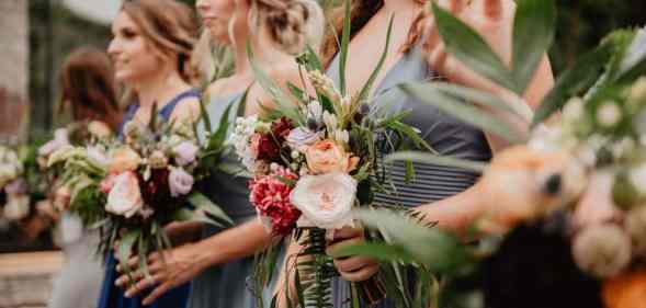 Several white women are standing next to each other while holding flowers as they act as bridesmaids in a wedding