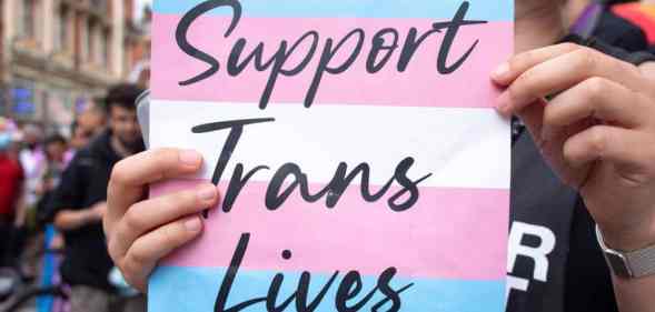 A placard that says 'support trans lives' printed against the transgender pride flag during a march