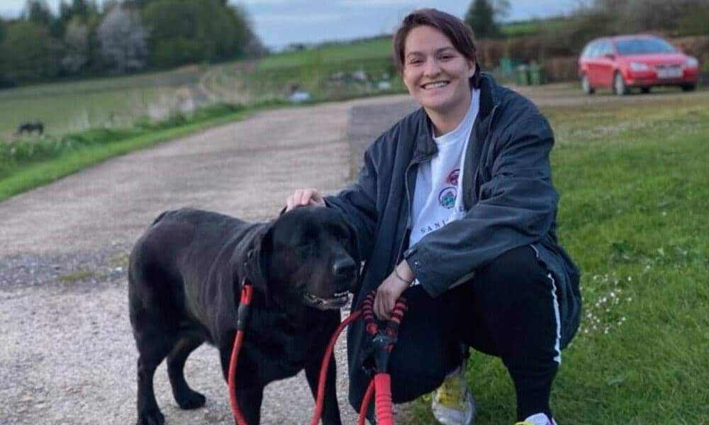 Tea Kane crouches next to a black dog and holds a red lead