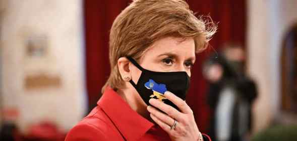 Scotland's first minister Nicola Sturgeon wearing a red jacket and a black face mask
