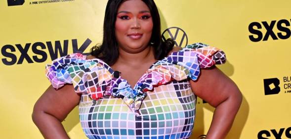 Lizzo wears a colourful, rainbow block outfit as she stands in front of a yellow background with the black SXSW logo on it