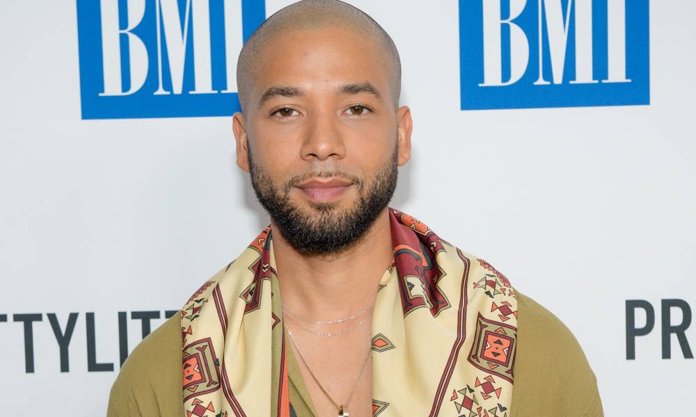 Jussie Smollett looks at the camera while wearing a light brown top and a patterned scarf around his neck