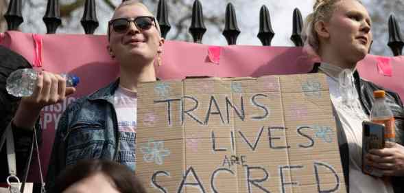 two people hold up a sign that reads 'trans lives are sacred'