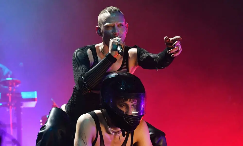 Years and Years singer Olly Alexander points at the crowd while singing into a microphone and straddling another person wearing a motorcycle helmet