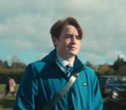 A still from Netflix's Heartstopper which shows Kit Connor as Nick Nelson wearing his school uniform and light blue coat