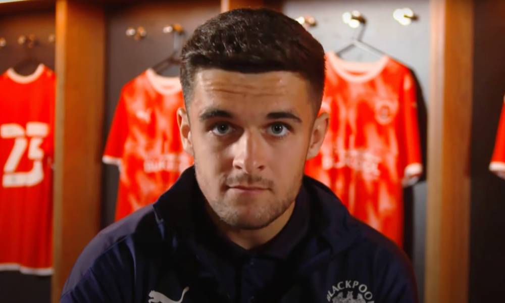 Blackpool football star Jake Daniels stares at the camera with football uniforms in the background