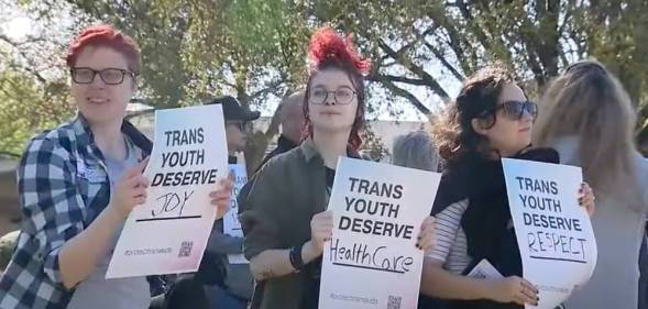 three people hold up signs that read "trans youth deserve joy", "trans youth deserve healthcare" and "trans youth deserve respect"